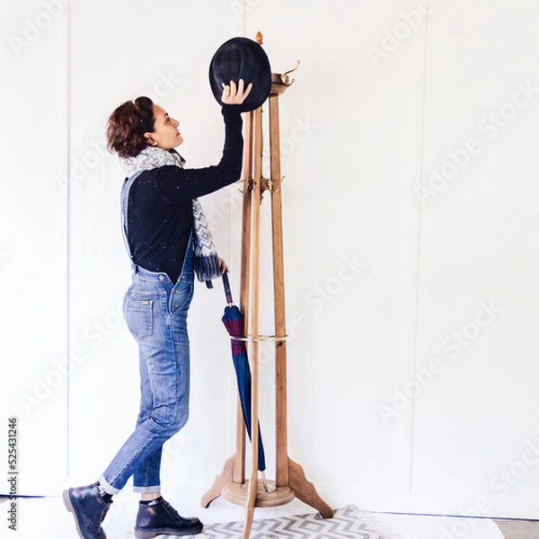 Obraz Portrait of a Caucasian woman next to a wooden coat rack hanging her clothes in a brigh and white room