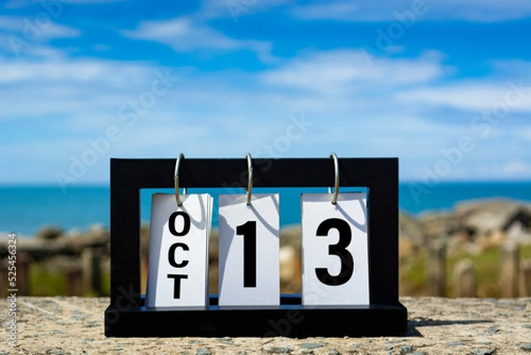 Fototapeta Oct 13 calendar date text on wooden frame with blurred background of ocean.