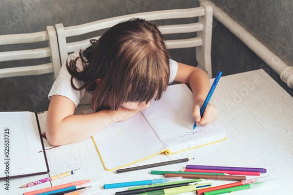 Fototapeta Girl sitting at the table and writing in a notebook