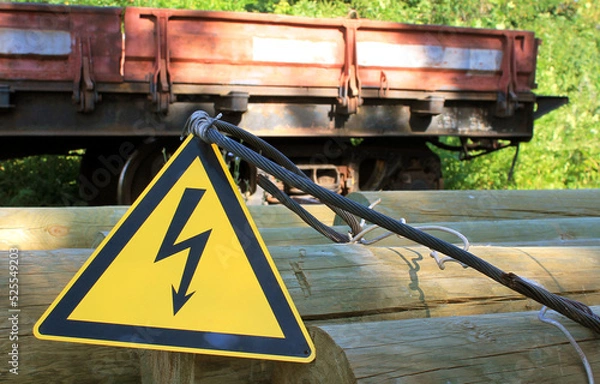 Fototapeta Caution electricity sign on wooden bars against the background of a railway cargo platform, High voltage icon, danger symbol, Attention, electricity danger symbol, electricity warning triangular symbo