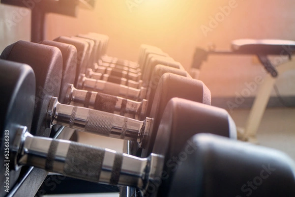 Fototapeta Close-up shot of dumbbells set on a shelf inside an empty workout gym against a backdrop of light from a window.