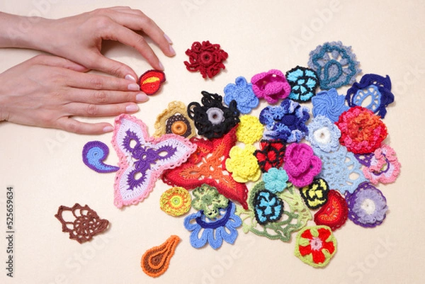 Fototapeta Lots of crocheted elements, colored knitted flowers on a beige background. Lays out a woman's hand