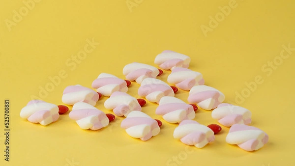 Fototapeta Marshmallows and red candy dragees in the form of a triangle on a yellow background