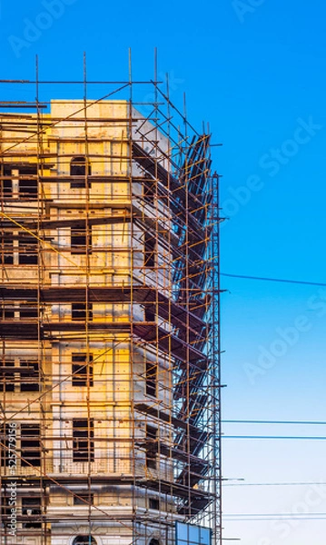 Fototapeta site scaffolding Apartment building under construction on a sunny day Multi-storey residential wooden structure street tlong exposure car