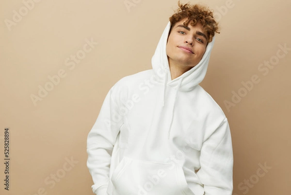 Fototapeta a cute, attractive man stands in a white hoodie and looks pleasantly into the camera. Horizontal photo with an empty space for inserting an advertising layout