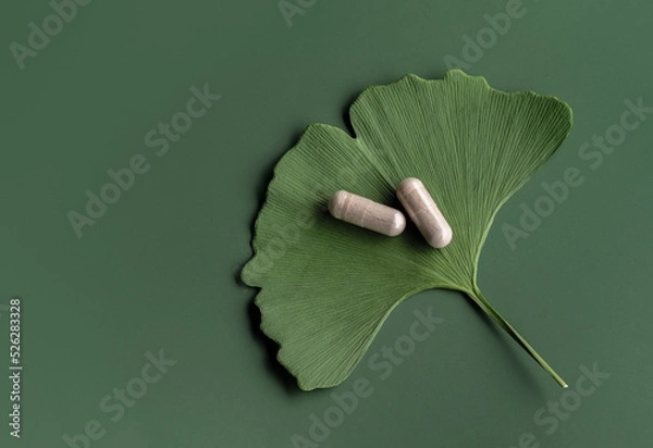 Fototapeta Ginkgo leaf with pills for brain, memory protect therapy and treatment of dementia. Ginkgo Biloba composition on green background, natural ingredient for alternative medicine, top view.