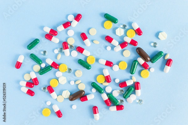 Fototapeta Pills of different shapes and colors are scattered on a blue background