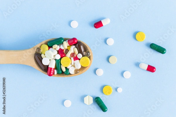 Fototapeta Top view of a wooden spoon filled with various pills on a blue background