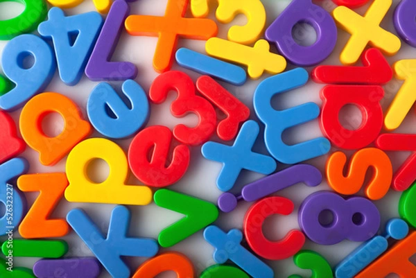 Fototapeta Plastic multi-colored alphabets letters on a magnet.
Lots of сolorful letters scattered on a white background. The concept of elementary school background texture for children. Top view closeup.