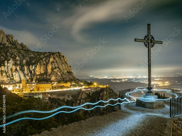 Fototapeta Paisaje nocturno de la montaña de Montserrat con fondo iluminado de poblaciones en Cataluña (España).