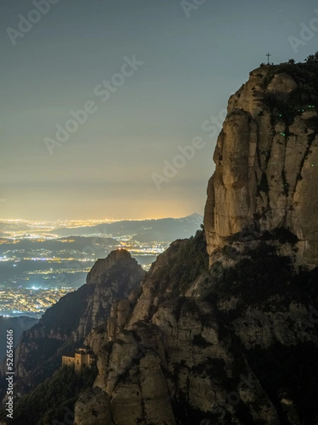 Fototapeta Paisaje nocturno de la montaña de Montserrat con fondo iluminado de poblaciones en Cataluña (España).