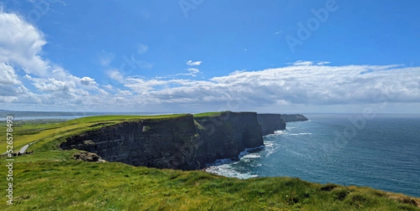 Fototapeta Panoramic view of the Cliffs of Moher sightseeing spot in Ireland under a cloudy blue sky and irish green grass