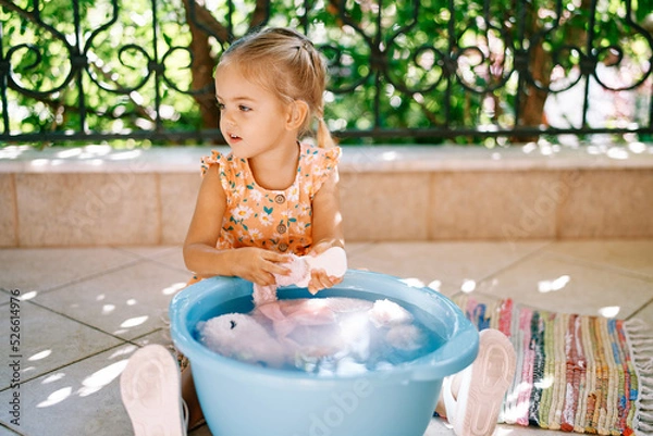 Fototapeta Little girl washes a soft toy on the balcony. High quality photo