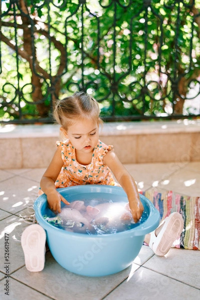 Fototapeta Little girl washes a soft toy in a bowl on the balcony. High quality photo