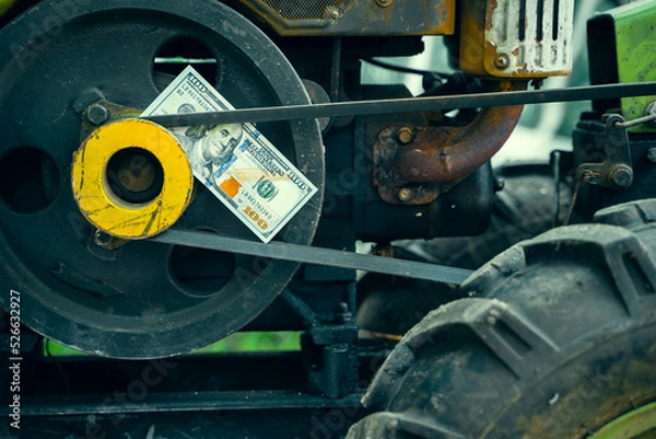Fototapeta A hundred dollar bill lies on the engine of a small rural walk-behind tractor for tillage