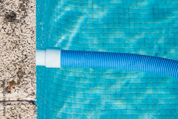 Fototapeta A connected blue pool cleaner hose floats in the pool water next to the stone curb. Pool cleaning and maintenance.
