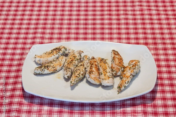 Fototapeta Presentation on a white plate of a delicious recipe for tender rosemary chicken tenderloins on a red checkered tablecloth.