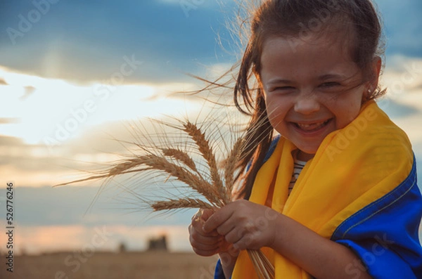 Fototapeta Child with Ukrainian flag. Girl with wheat in her hands. War in Ukraine. Wheat in children's hands. A child with a blue and yellow flag in the field. Export of Ukrainian grain. Peace concept. freedom