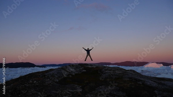 Fototapeta Person silhouette jumping in the air with icebergs in the back in Greenland