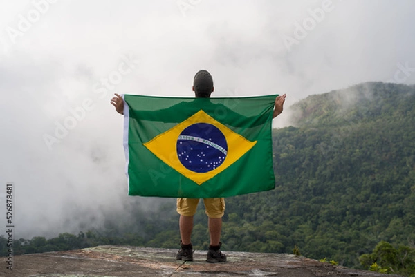 Fototapeta Young Man at Mountain Looking to Horizon in Nature with brazilian Flag.