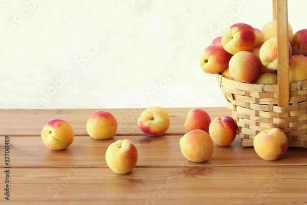 Fototapeta Apricots in wicker basket and scattered on the table isolated on white