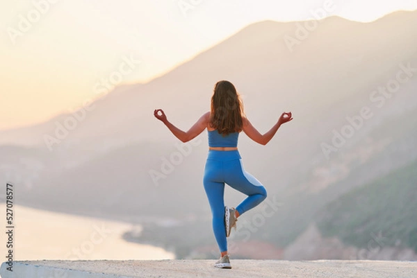 Fototapeta Inspired female enjoying of meditation on top with beautiful view at sunset time. Relief stress and clean healthy minds