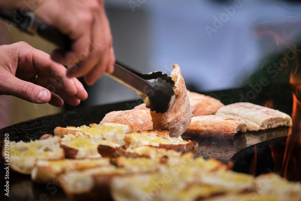 Obraz close-up detail view of chef flipping sandwiches grilled at round steel iron firepit hearth table surface brazier, red fire, barbecue