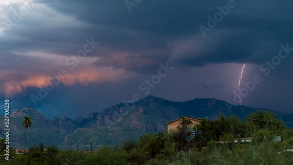 Fototapeta Lightning bolt and monsoon storm clouds over the Catalina Mountains in the Sonoran Desert north of Tucson, Arizona. Beautiful colorful moody sky, windmill, houses and natures furious beauty.
