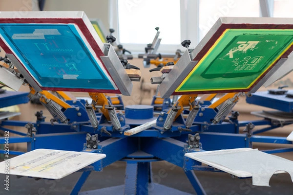 Fototapeta Serigraphy silk screen print process at clothes factory. Frame, squeegee and carousel.
