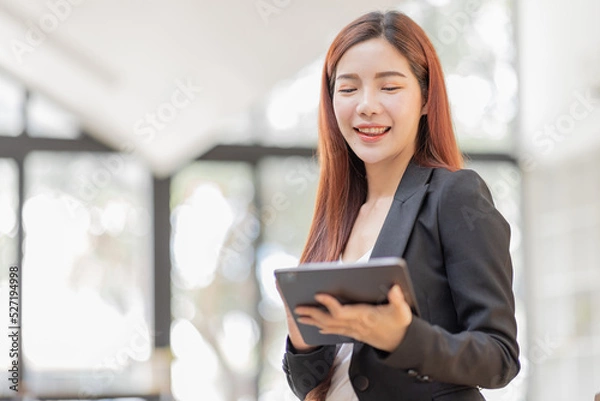 Fototapeta Business Asian Female holding tablet laptop and steanding in the workplace, concept of business accounting documents planning finance analysis and report,	