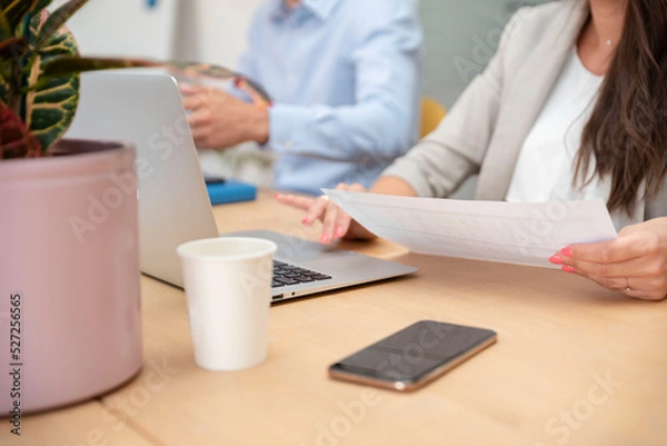 Obraz Close-up of unrecognizable businesswoman sitting at the table in front of laptop and holding a document in her hand
