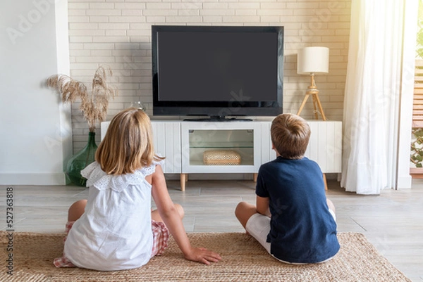 Fototapeta Two children sitting on the living room floor watching television. Mock up for inserting images in the tv