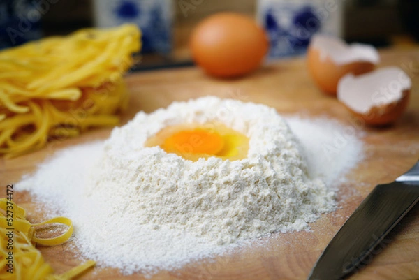 Fototapeta On the table is flour with an egg for Italian pasta. Homemade food. Rustic.