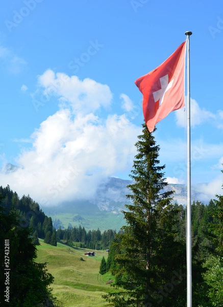 Fototapeta Swiss flag in cloud covered mountains