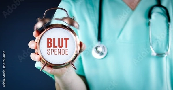Fototapeta Blutspende. Arzt zeigt Wecker/Uhr mit Text. Hintergrund blau.