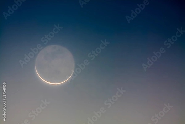 Fototapeta Crescent moon showing earthshine at dawn