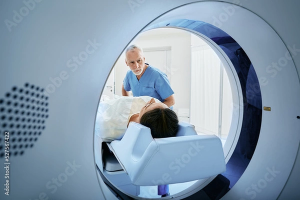 Fototapeta CT scan technologist overlooking patient in Computed Tomography scanner during preparation for procedure. Woman patient going into CT scanner
