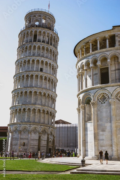 Fototapeta Pisa, Toscana , Italia 08-28-2022.  A picturesque portrait shot of the famous Pisa Leaning Tower on a beautiful day at dusk with a blue sky, and the sun shines on the white marbled campanile.