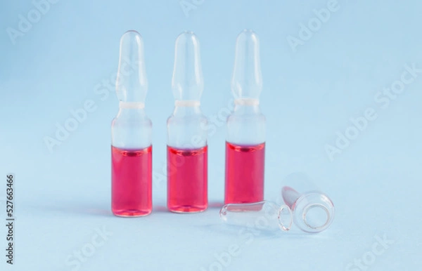 Fototapeta three ampoules on a blue background with pink liquid and one ampoule is empty
