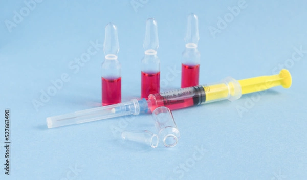 Fototapeta on a blue background, a syringe with pink liquid, three ampoules with liquid and an empty ampoule