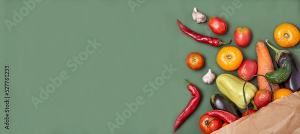 Fototapeta Trendy ugly organic vegetables. Assortment fresh bell peppers, tomatoes, eggplants, hot peppers, carrots, cucumbers in craft paper bag over green background. Top view. Non gmo. Banner with copy space