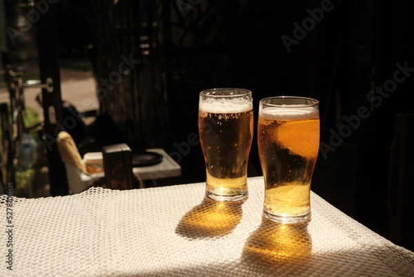 Fototapeta Two glasses of cold beer on the table of street cafe, beautiful shadows from bright sunlight. Copy space.