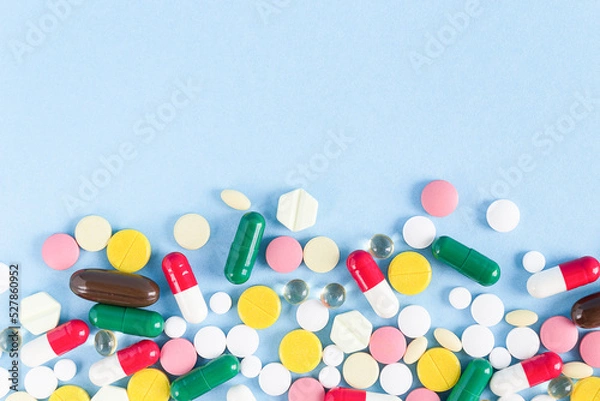 Fototapeta Pills of different shapes and colors are scattered on a blue background