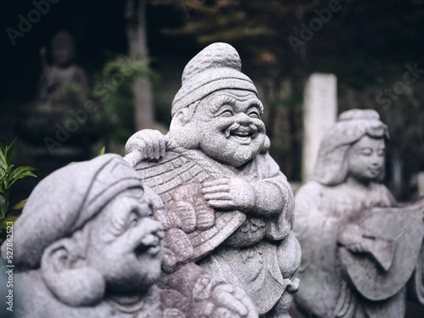 Fototapeta stone statue of laughing Ebisu, one of the japanese seven lucky gods in a quiet temple of tokyo with a dark background