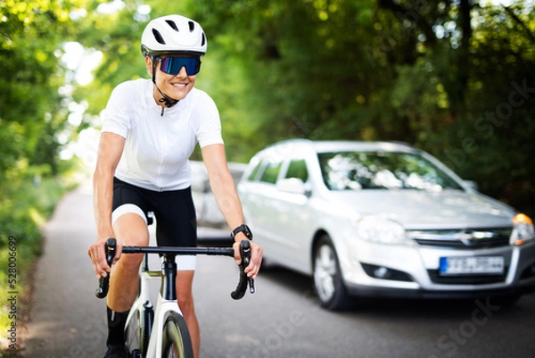 Fototapeta Radfahrerin auf einem Rennrad wird auf einer Landstraße von einem Auto überholt 