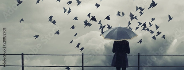 Fototapeta Woman with umbrella standing on the rain during autumn storm and watching flock of birds fly	