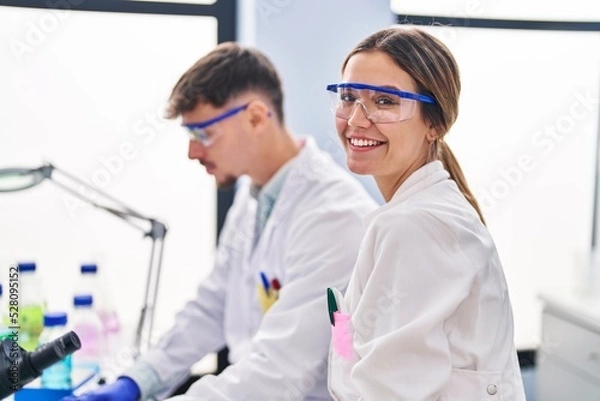 Fototapeta Young man and woman scientists workers using laptop working at laboratory