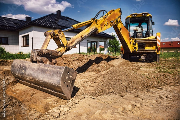 Fototapeta Excavator working at house construction site - digging foundations for modern house. Beginning of house building. Earth moving and foundation preparation.