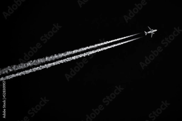 Fototapeta Twin-engined jetliner with contrails flying in black sky
