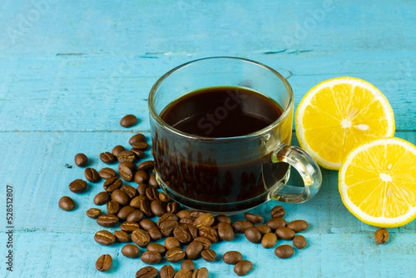 Fototapeta Black coffee in transparent glass with fresh lemon and coffee bean on blue wooden background. Espresso romano drink for healthy.